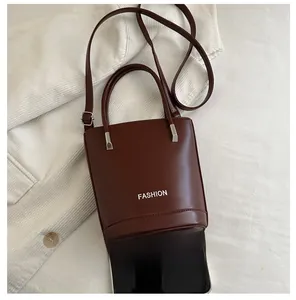 Detail of dark brown leather bucket bag with top handles and adjustable strap on soft fabric