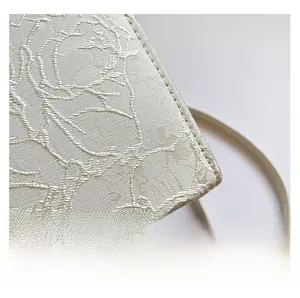 Close-up of white floral jacquard fabric with detailed 3D texture on a woman handbag