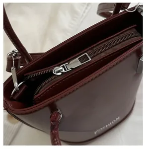 Close-up of smooth silver zipper closure on deep red leather bucket bag with texture