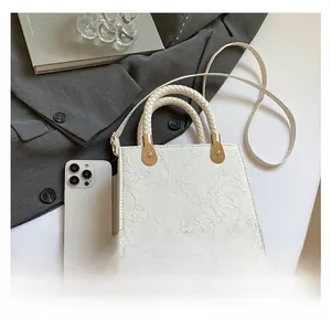 Detail of white crossbody bag with floral embossed texture and woven top handle
