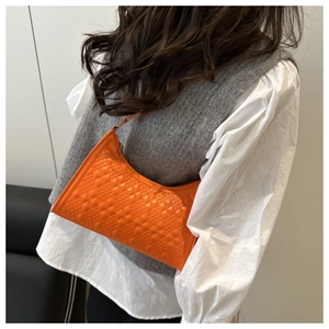 Detail of orange quilted crescent shoulder bag with elegant geometric texture on model