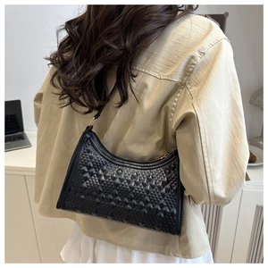 Detail of black baguette bag with diamond embossed texture worn by a model in a modern room