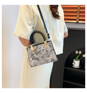Detail of floral printed handbag with black woven handle and gold hardware on a model