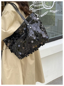 Detailed view of black sequined tote bag with leather handles in urban outdoor setting