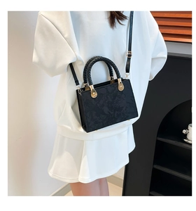 Detail of black jacquard crossbody bag with woven handle and gold hardware on model