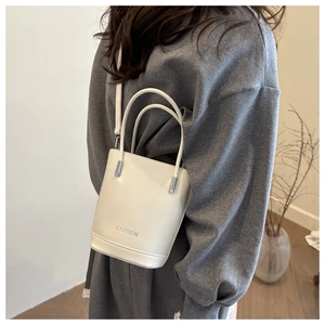 Detail of a beige bucket bag with silver hardware worn by a model in a modern interior