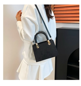 Side view of black crossbody bag with textured handle and gold metal hardware on model