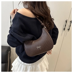 Détail du sac à bandoulière marron foncé avec motif texturé et nœud argenté sur un modèle