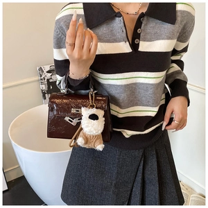 Détail d'un sac à main en cuir verni marron foncé avec un charm de poupée en peluche blanche