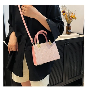 Detailed view of pink floral embossed handbag featuring a woven top handle and metal feet