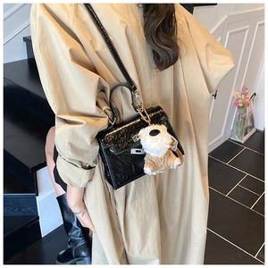Détail du sac bandoulière en cuir noir brillant avec breloque ours et boucle métallique