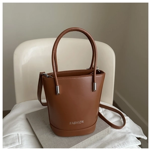 Detail of a brown bucket bag with silver Fashion logo, top handles and thin strap