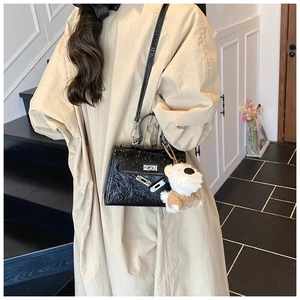 Détail du sac à main noir brillant avec fermoir argenté et charm de chiot en peluche blanc