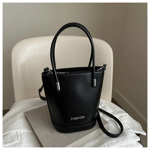 Detail of a black bucket bag with a silver fashion logo on a minimalist background