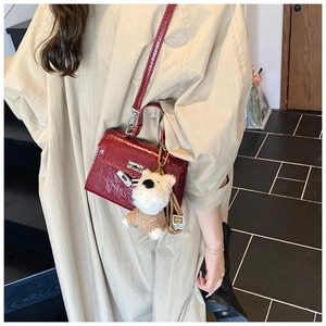 Détail d'un sac à main en cuir verni rouge foncé avec fermoir en métal et charm chien
