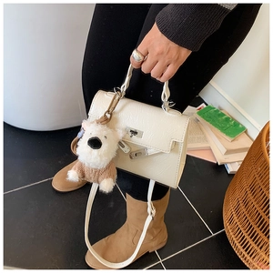 Détail d'un sac à main en cuir crème avec fermoir métallique et charm ours en peluche décoratif
