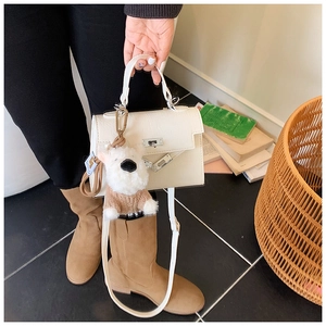 Détail du sac à main blanc crème avec breloque en peluche et élégant fermoir doré tournant