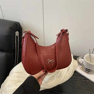 Borsa hobo intrecciata rosso scuro con fiocco in metallo, tenuta a mano su sfondo studio