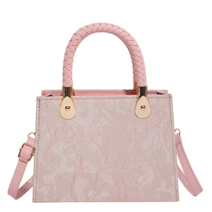 Pink woven floral handbag with gold hardware and adjustable strap on white background