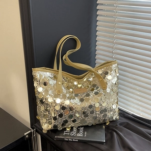 Chic gold sequin tote bag with leather handles shown against a stylish studio backdrop