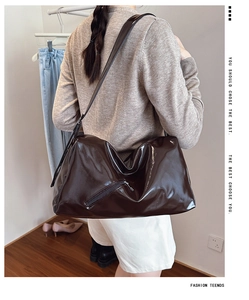 Detail of dark brown patent leather tote bag showing side zipper and shiny texture