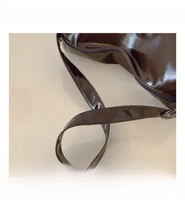 Detail of the high-shine brown leather tote bag showing handle stitching and zipper closure