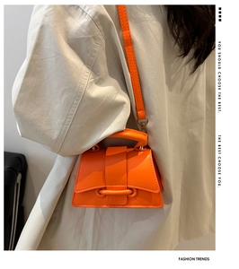 Détail d'un mini sac à main orange vif avec boucle épaisse sur un blazer crème