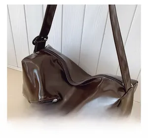 Close-up of a large dark brown polished leather tote bag featuring side zipper details
