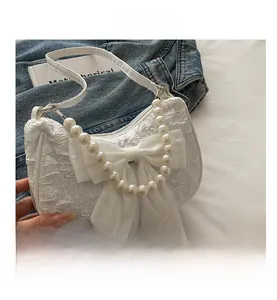 Detail of white pleated handbag featuring a large chiffon bow and pearl handle ornament