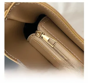 Détail de la fermeture éclair dorée et des surpiqûres blanches sur le sac marron