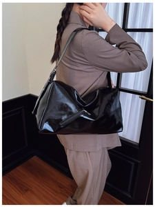 Detail of glossy black faux leather tote bag with stylish zipper on model in beige blazer