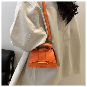 Petit sac bandoulière orange porté par un mannequin avec une chemise beige chic
