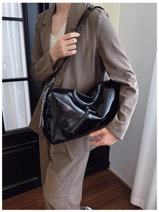Detail of a black glossy leather tote bag showing side zipper and smooth texture