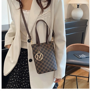 Close-up of retro monogram bucket bag with gold M pendant and detachable leather strap