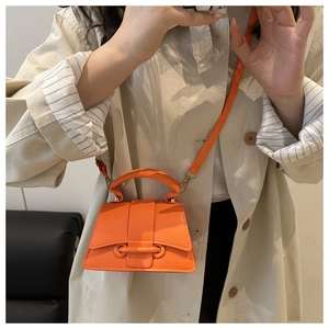 Gros plan d'un mini sac à main orange vif en cuir texturé porté avec un trench beige