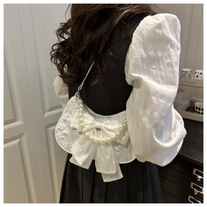 Detailed texture of white lace shoulder bag with large satin bow and pearl handle