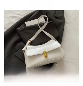 Detail showing the white patent leather surface and golden cylinder buckle on the shoulder bag