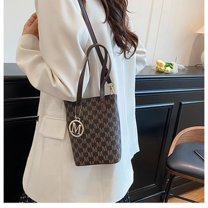 Detailed view of a brown monogram tote bag with gold M charm worn with a white blazer