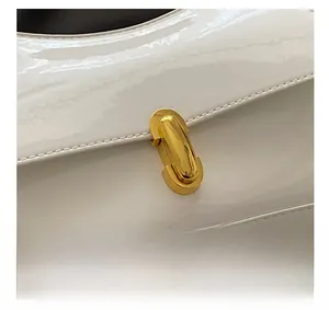 Detailed close-up of a white patent leather bag featuring a polished gold metallic buckle