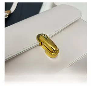 Detailed macro view of the premium golden capsule-shaped buckle on white leather bag