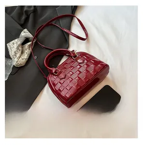 Detail view of wine red patent leather shell bag with quilted texture and glossy finish