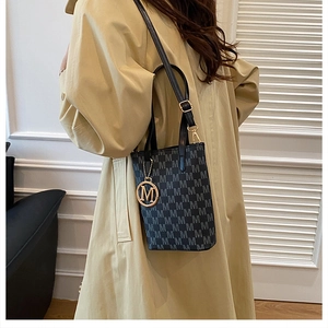 Vue détaillée du mini sac cabas noir à monogramme avec pendentif doré et bandoulière chic