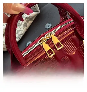 Detail of burgundy patent leather shell bag with gold double-way zipper and embossed grid