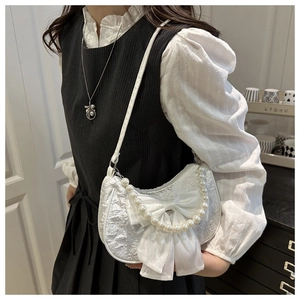 White jacquard half-moon bag with large bow and pearl chain detail worn by a model