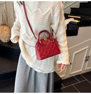 Detail of dark red woven shell bag with glossy finish and gold zipper on crossbody strap