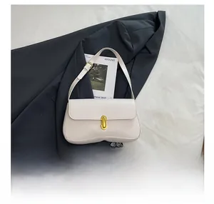 Flat lay of white faux leather underarm bag with gold clasp on white fabric with props