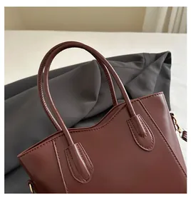 Détail du sac cabas en cuir brun rouge avec coutures renforcées et anneau doré