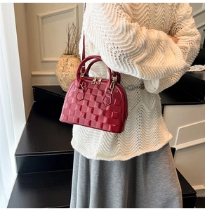 Detail of burgundy shell bag showing embossed texture and gold zipper closure