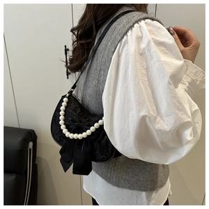 Close-up of black lace shoulder bag featuring a silk bow and decorative pearl strap