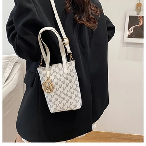 Detail of elegant cream-colored crossbody bag with monogram pattern and gold M pendant